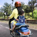 Mother and child riding scooty with navy blue baby safety belt harness providing secure support for toddler on 2-wheeler vehicle.