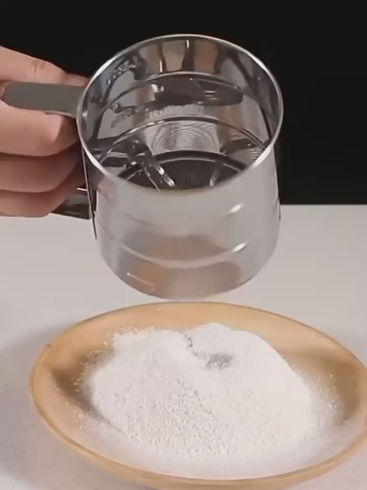 Demonstration video of stainless steel flour sifter with manual press handle, showing how to sift flour onto a plate for baking and cooking