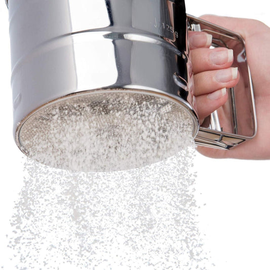 Close-up of stainless steel flour sifter with manual handle, sifting flour through a fine mesh for baking, perfect kitchen sieve for atta, sugar, cocoa, and powdered ingredients