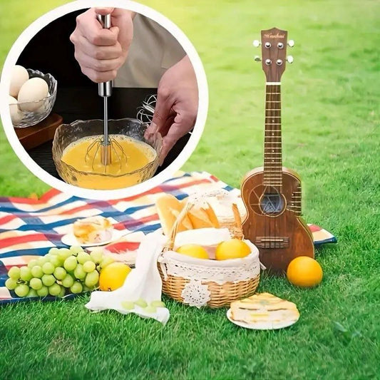 Steel hand press blender shown whisking eggs, with a picnic setup featuring fruit, bread, and a guitar, highlighting its versatility for kitchen and outdoor use